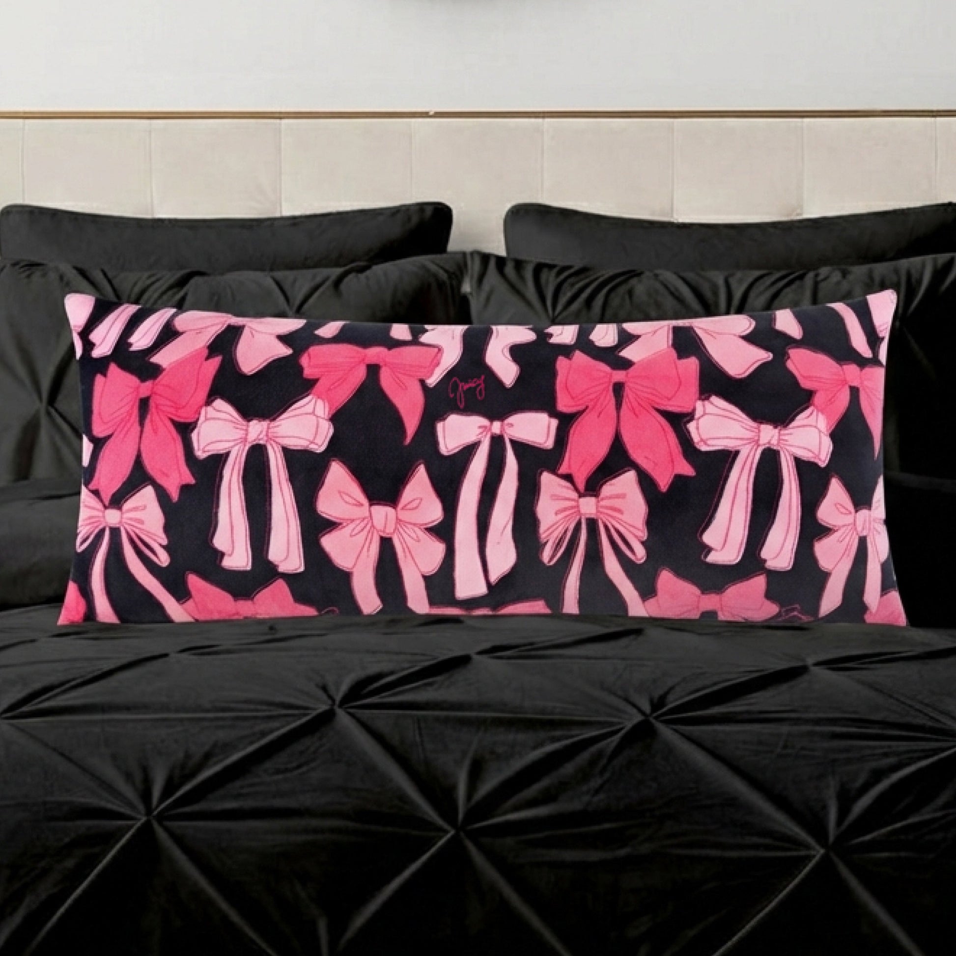 The Plush Body Pillow features an oversized, plush design with various pink bows on a black background, resting on a textured black bedspread with matching pillows.