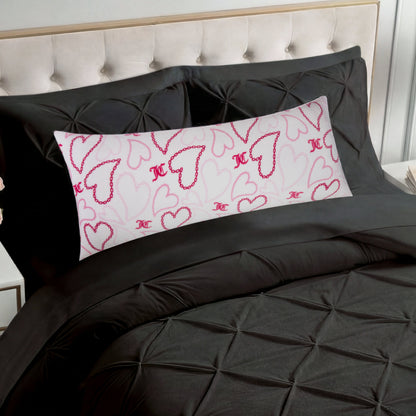 A bed with a black, textured comforter and matching pillows, featuring the Plush Body Pillow adorned with pink and red outlined hearts and a script "K" pattern on a white background.