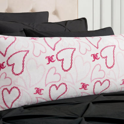 The Plush Body Pillow features pink heart and chain patterns and rests on a black bedspread, paired with black pillows and a beige upholstered headboard.