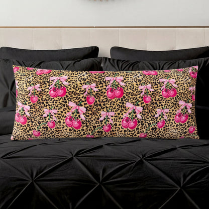 A Plush Body Pillow featuring a leopard print with bright pink cherries and pink bows, shown on black bedding and a cream-colored headboard.
