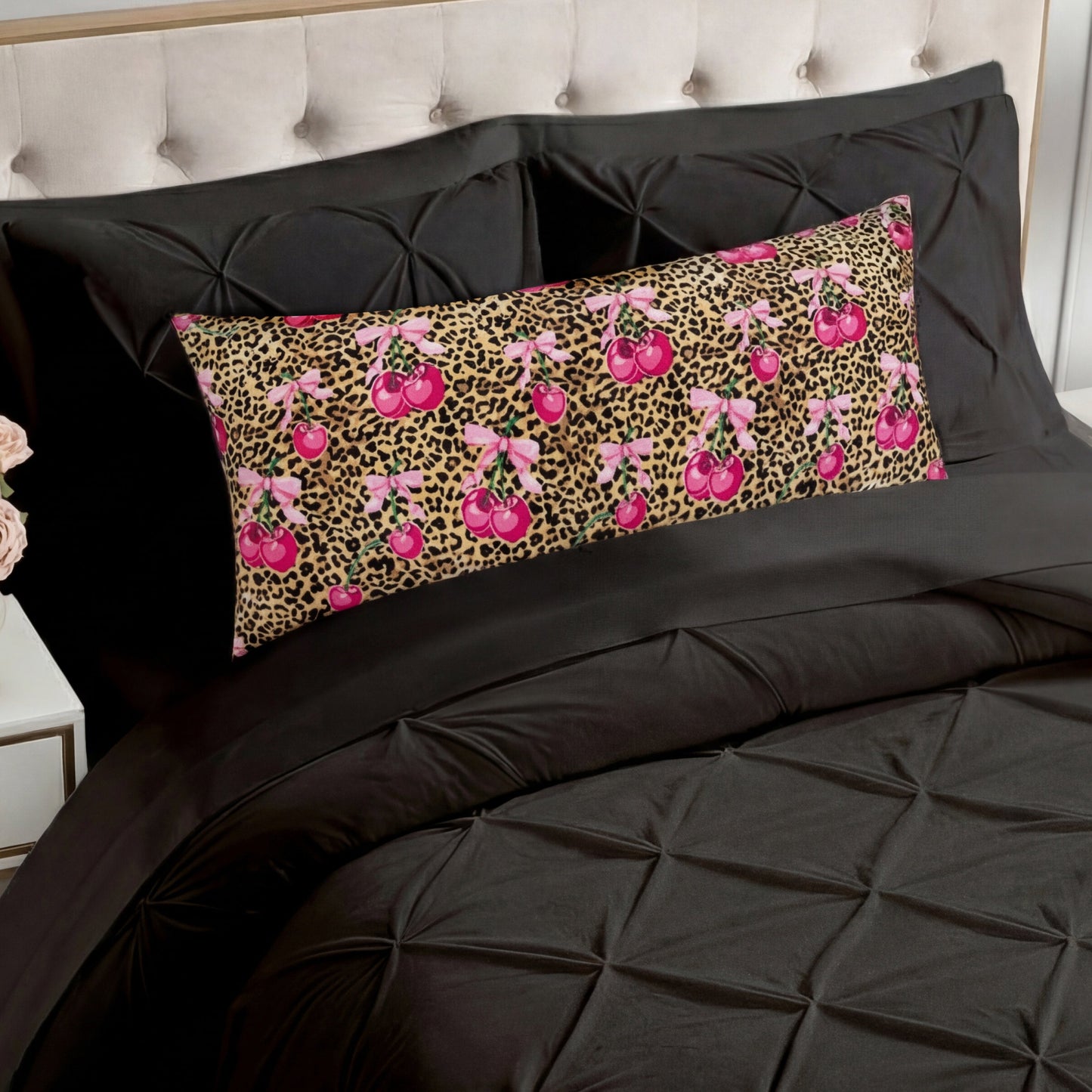 A bed with black tufted bedding and a Plush Body Pillow rests before a beige tufted headboard, featuring a leopard print background with pink cherry patterns.