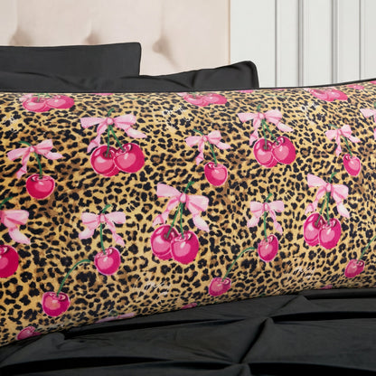 The Plush Body Pillow features a leopard print background with bright pink cherries tied with light pink bows, and is shown resting on a black bed with matching black pillows.