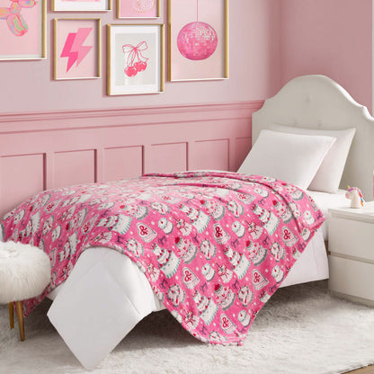 A pink Kids Plush Throw Blanket adorns a neatly made bed with a white headboard and pillow, beside a side table in a pink-themed bedroom featuring framed artwork and a fluffy white stool. Ideal for those who love playful, cozy decor.