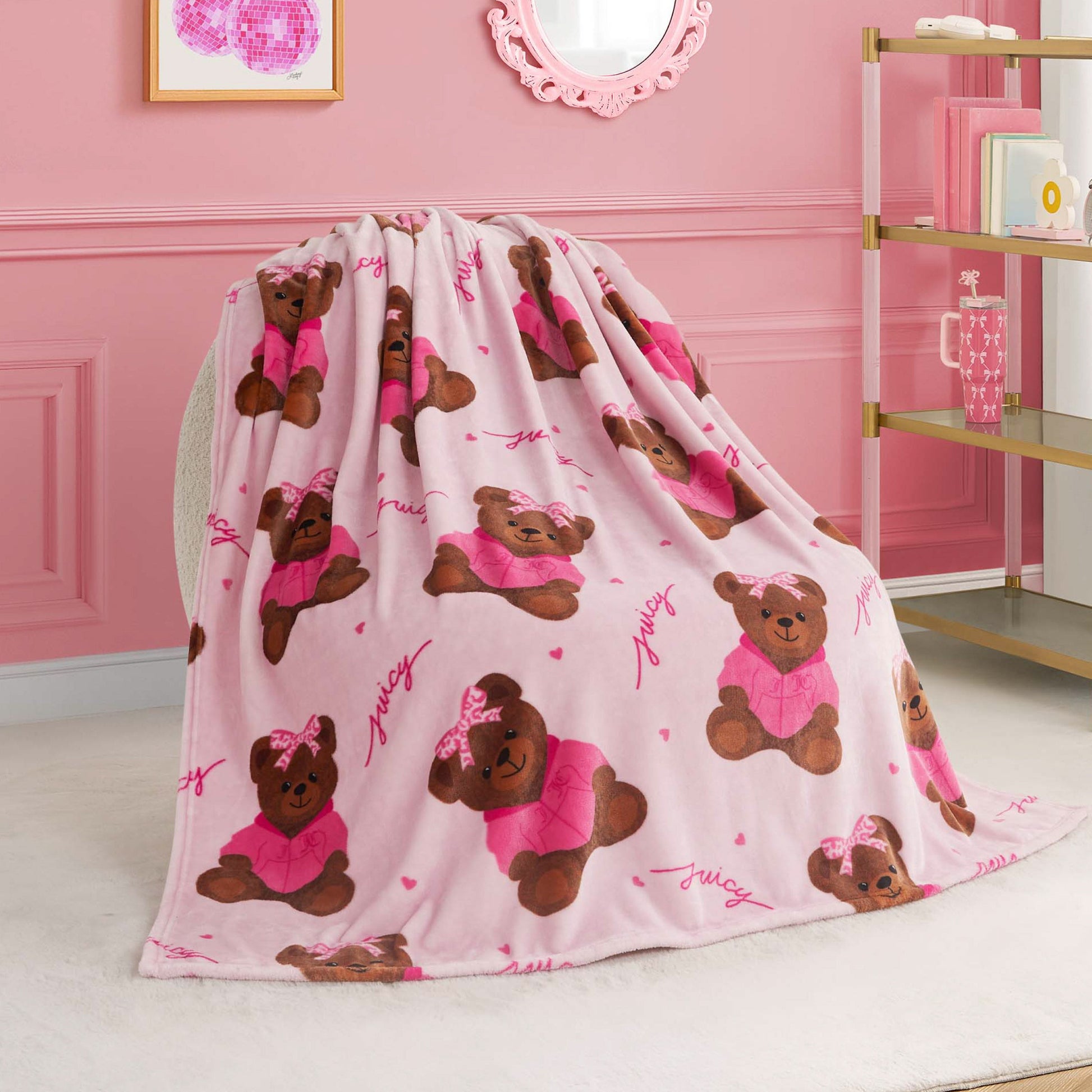 A Kids Plush Throw Blanket in pink, decorated with adorable brown teddy bears in pink outfits and bows, is draped over a chair in a stylish room. This ultra-soft blanket adds cozy charm to shelves, wall art, and mirror accents.