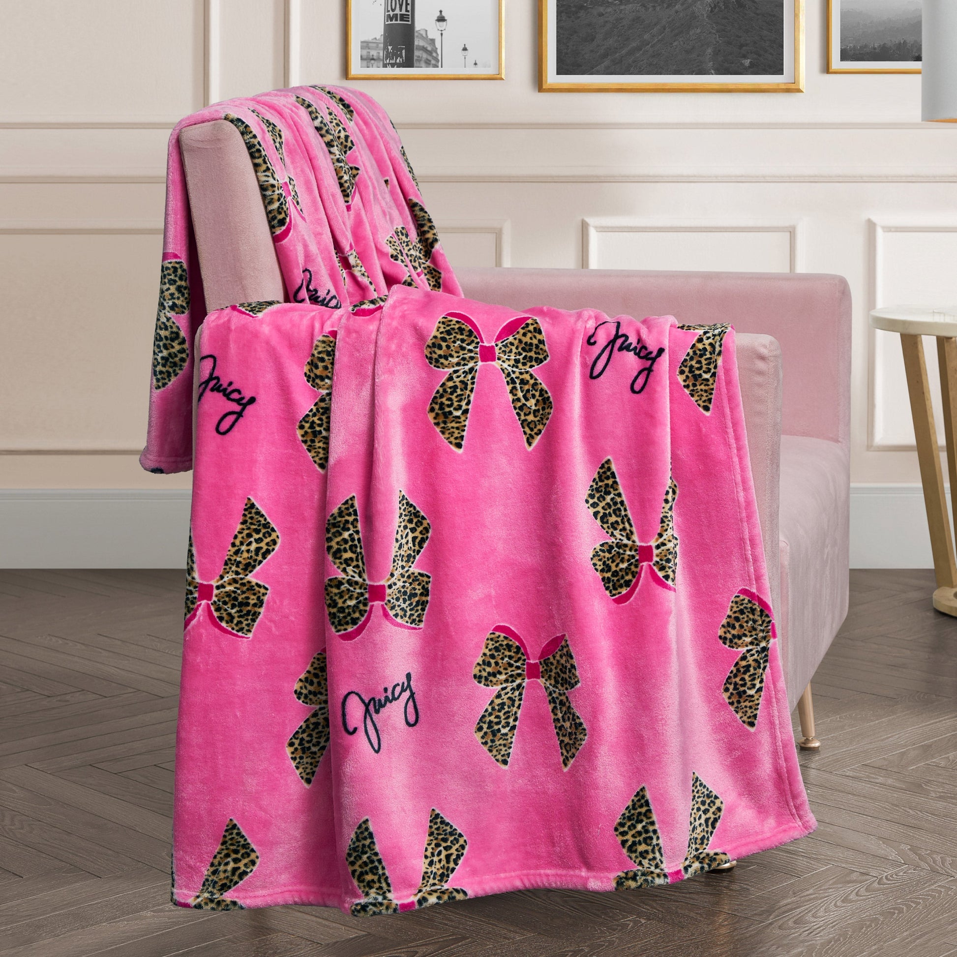 A Plush Oversized Throw Blanket in pink with leopard-print bows and “Juicy” in black script is draped over a pale pink armchair, bringing a cozy vibe to this modern living room.