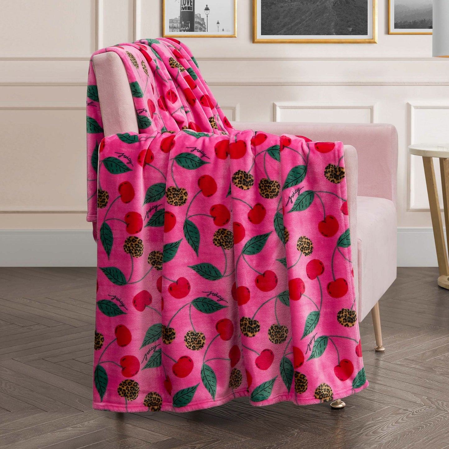 The Plush Oversized Throw Blanket, adorned with red cherries, leopard print circles, and green leaves, is draped over a light pink armchair in a modern living room—an ultra-soft choice for cozy nights.