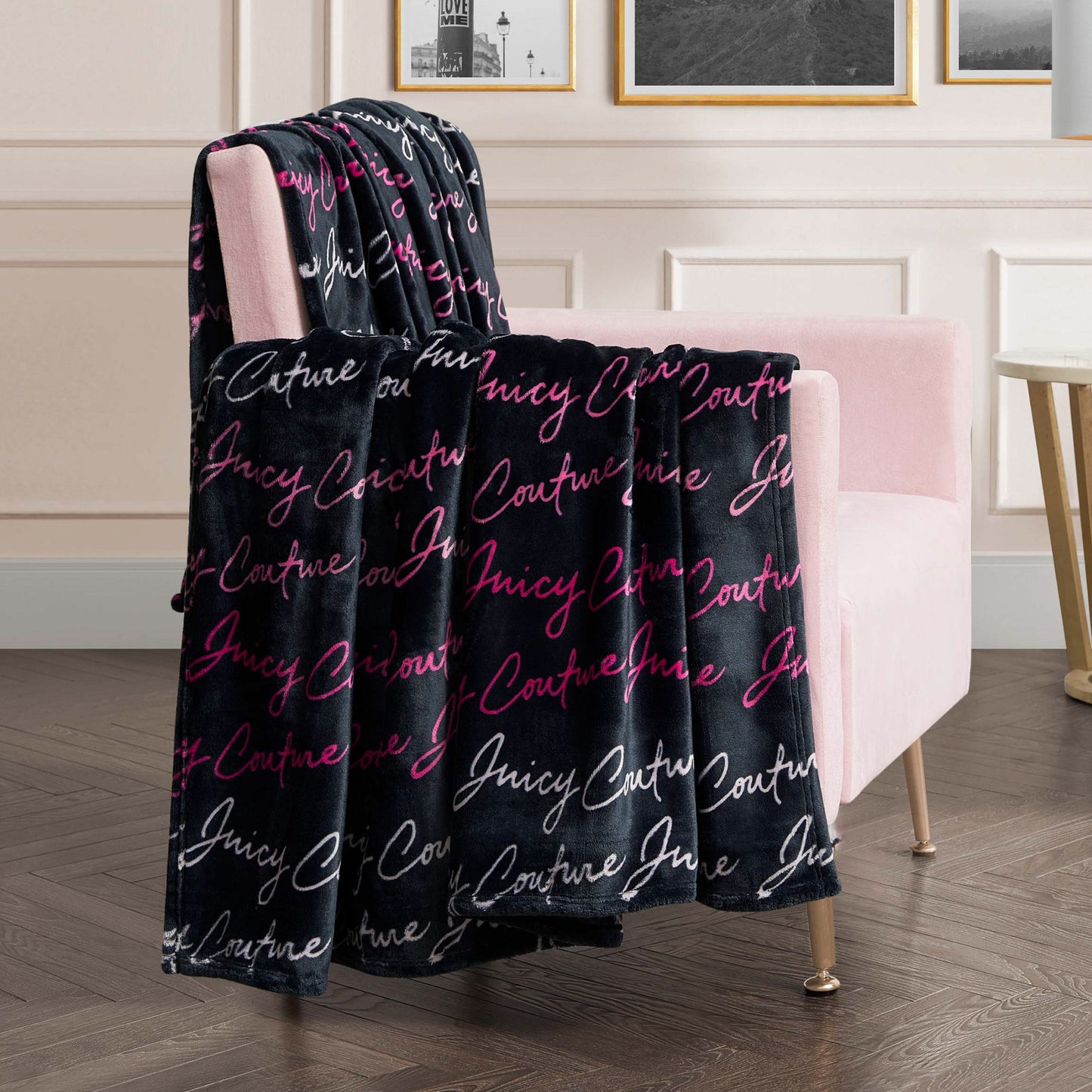 A Plush Oversized Throw Blanket, ultra-soft and pink with white script, is draped over a pale pink armchair in a modern living room decorated with framed art.