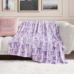 A white couch with a pink Juicy Couture pillow and a Plush Oversized Throw Blanket, light purple with bows and butterflies, draped over it. Behind the couch, framed black-and-white photos are displayed on the wall.