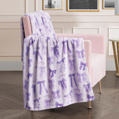 A Plush Oversized Throw Blanket is draped over a pale pink armchair in a modern living room decorated with framed pictures on a white wall.