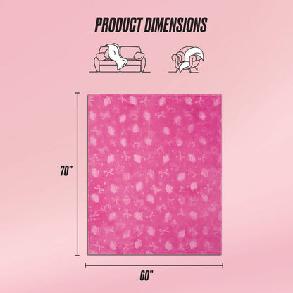 An Embossed Plush Oversized Throw Blanket by Juicy Couture, featuring a subtle fruit pattern, is shown on a light pink background. Measuring 70x60 inches, icons highlight its cozy comfort for use on the couch or by an individual.