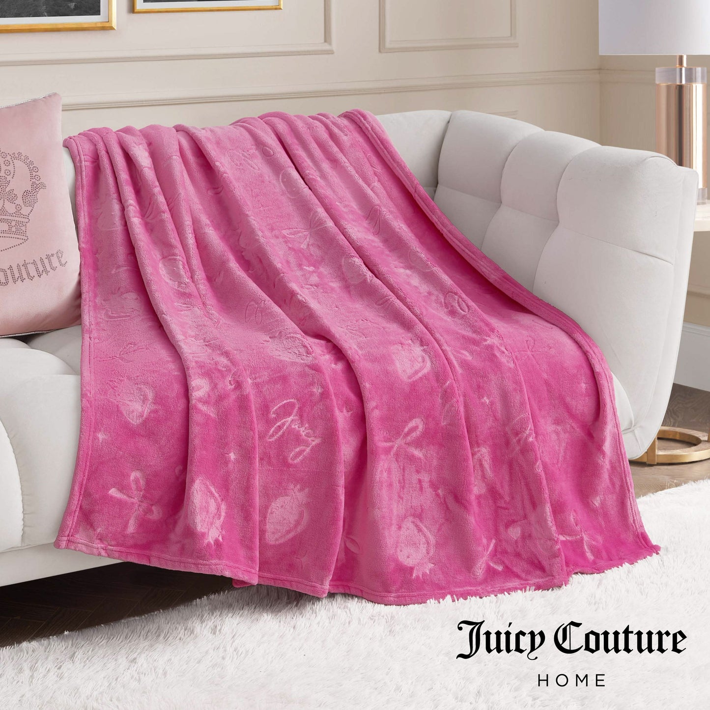 An Embossed Plush Oversized Throw Blanket in pink, featuring strawberries and bows, is draped over a white couch.