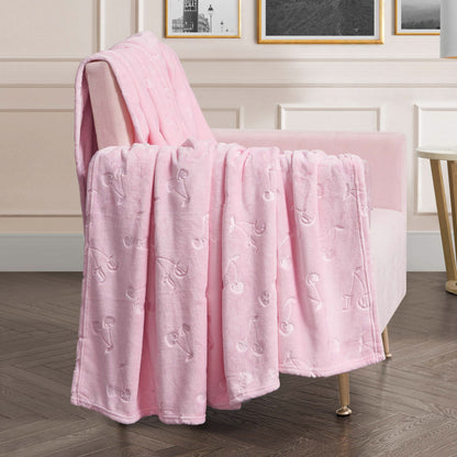 An Embossed Plush Oversized Throw Blanket in soft pink with a cherry pattern is draped over a light pink armchair in a chic room with white paneled walls, framed art, and a round side table.