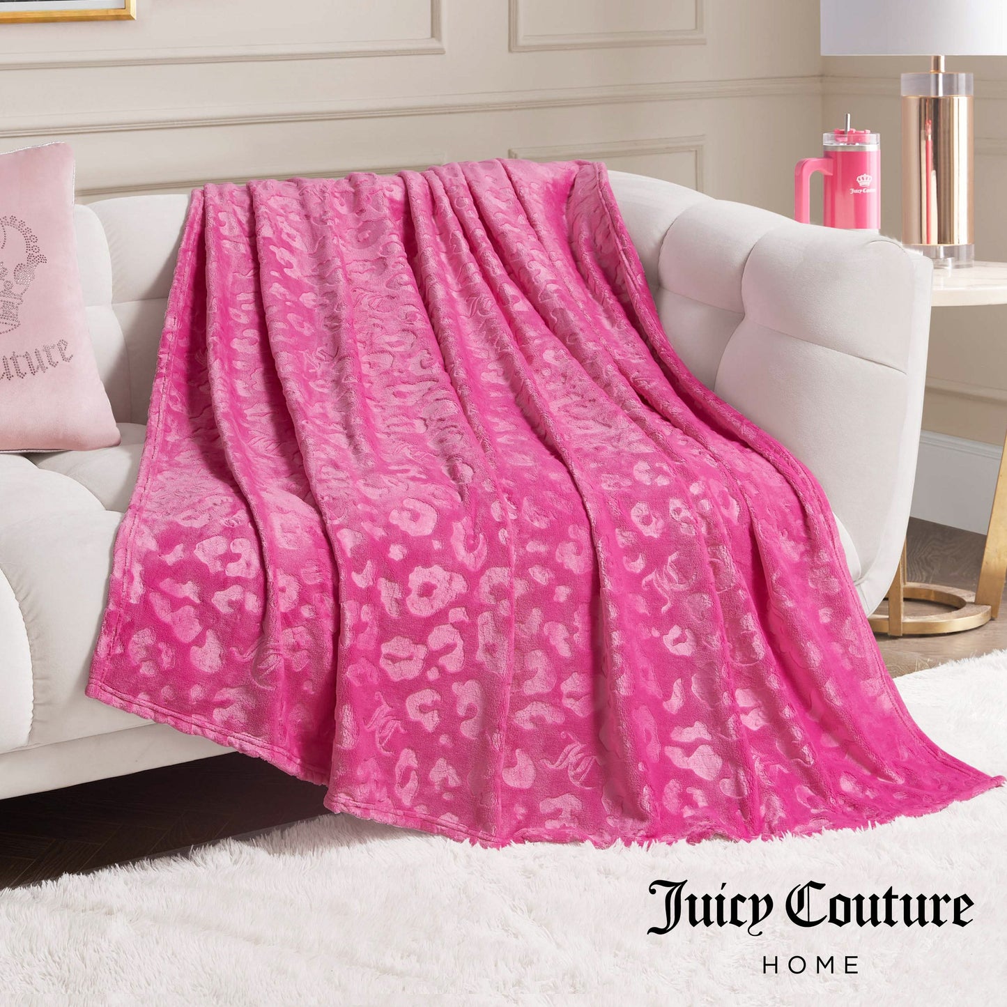 An Embossed Plush Oversized Throw Blanket in bright pink with a subtle leopard print is draped over a white sofa in a modern, stylish living room.