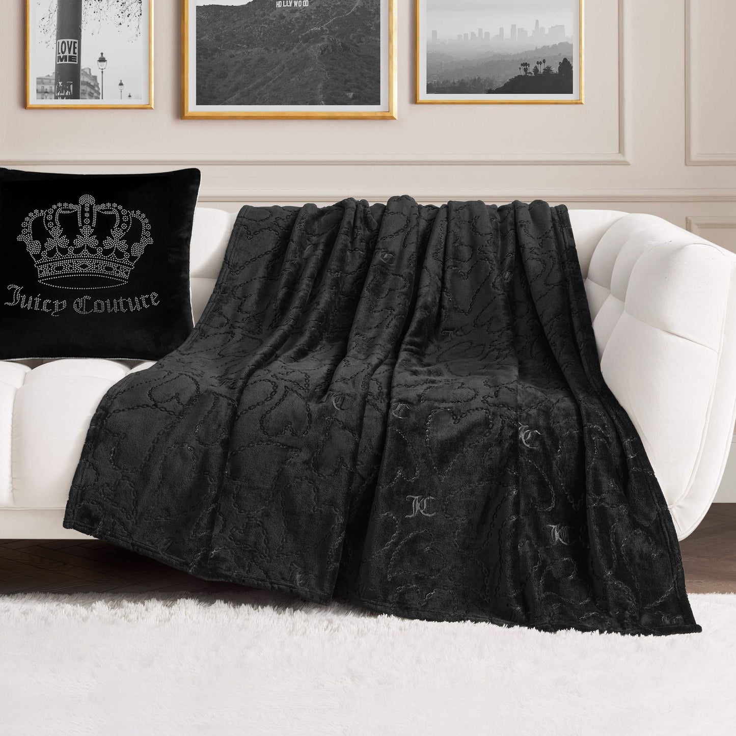 An Embossed Plush Oversized Throw Blanket in black is draped over a white sofa beside a matching black pillow, creating a stylish living room scene with framed wall art and a white rug.