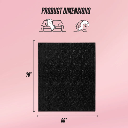 The Embossed Plush Oversized Throw Blanket by Juicy Couture is shown in black with a subtle heart pattern, measuring 70"x60". Versatile for use as a couch cover or wrap, it's displayed on a pink background with Product Dimensions text.