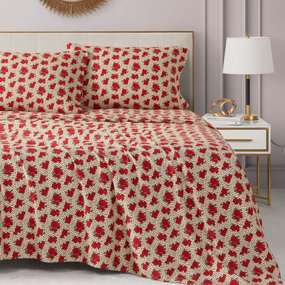 A neatly made bed with a red and white floral Printed Microfiber Sheet Set and matching pillows. The room has a modern nightstand with a white lamp, books, gold decor, and a sunburst mirror on a light-colored wall.