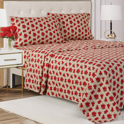 A neatly made bed with a cream and red floral-patterned Printed Microfiber Sheet Set and matching pillowcases, flanked by white nightstands with lamps and a vase of red roses. The room features modern decor and a tufted headboard.