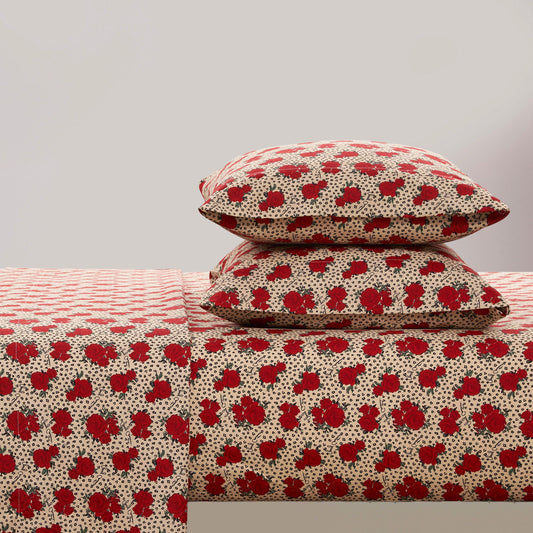 Two pillows and a bed, dressed in the Printed Microfiber Sheet Set with red roses and black dots on beige, create a chic look against a light gray backdrop—ideal for anyone who appreciates luxury bedding.