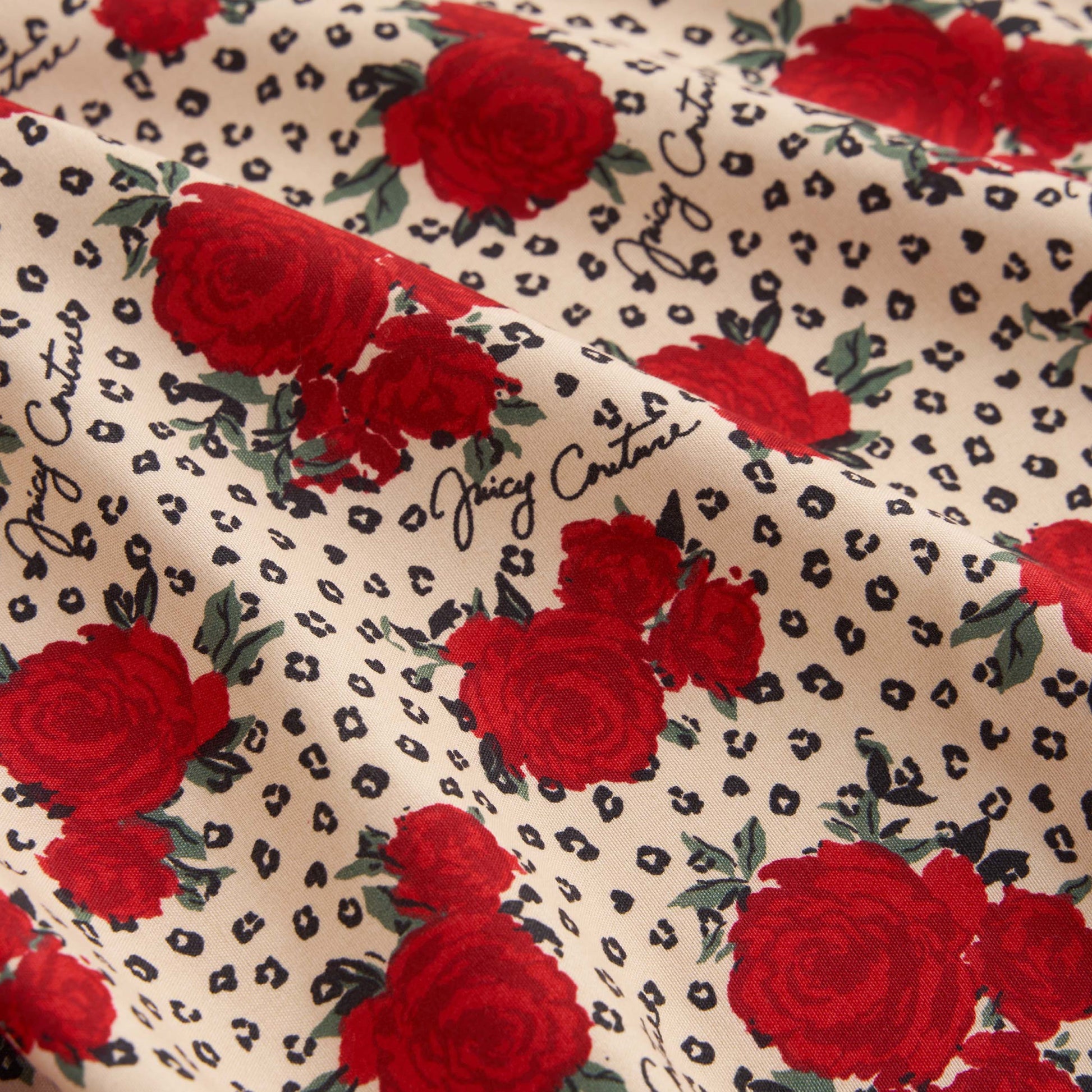 The Printed Microfiber Sheet Set features cream fabric with red roses, small black animal print spots, and "Juicy Couture" in cursive—an ideal choice to bring luxurious Juicy Couture style to your bedding.