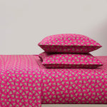 A bed with a bright pink Printed Microfiber Sheet Set and two matching pillows, all featuring a repeating pattern of small white and black hearts. The background wall is plain and light-colored.
