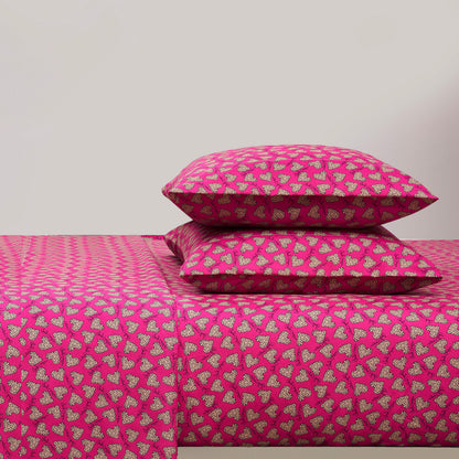 A bed with a bright pink Printed Microfiber Sheet Set and two matching pillows, all featuring a repeating pattern of small white and black hearts. The background wall is plain and light-colored.