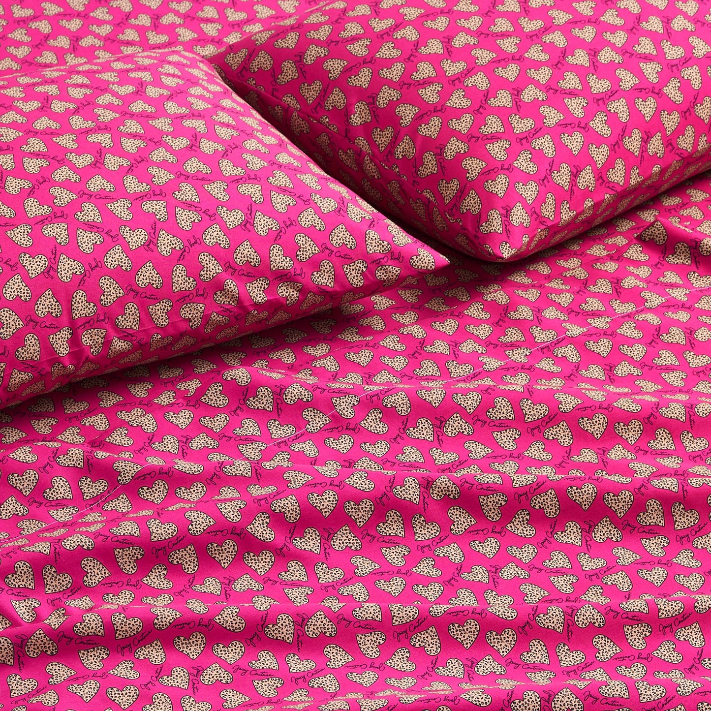 Close-up of a bed with a Printed Microfiber Sheet Set in bright pink, showcasing smooth fabric and a repeating pattern of small white polka-dotted hearts on the pillows and sheets—a vibrant, luxurious bedding accent.