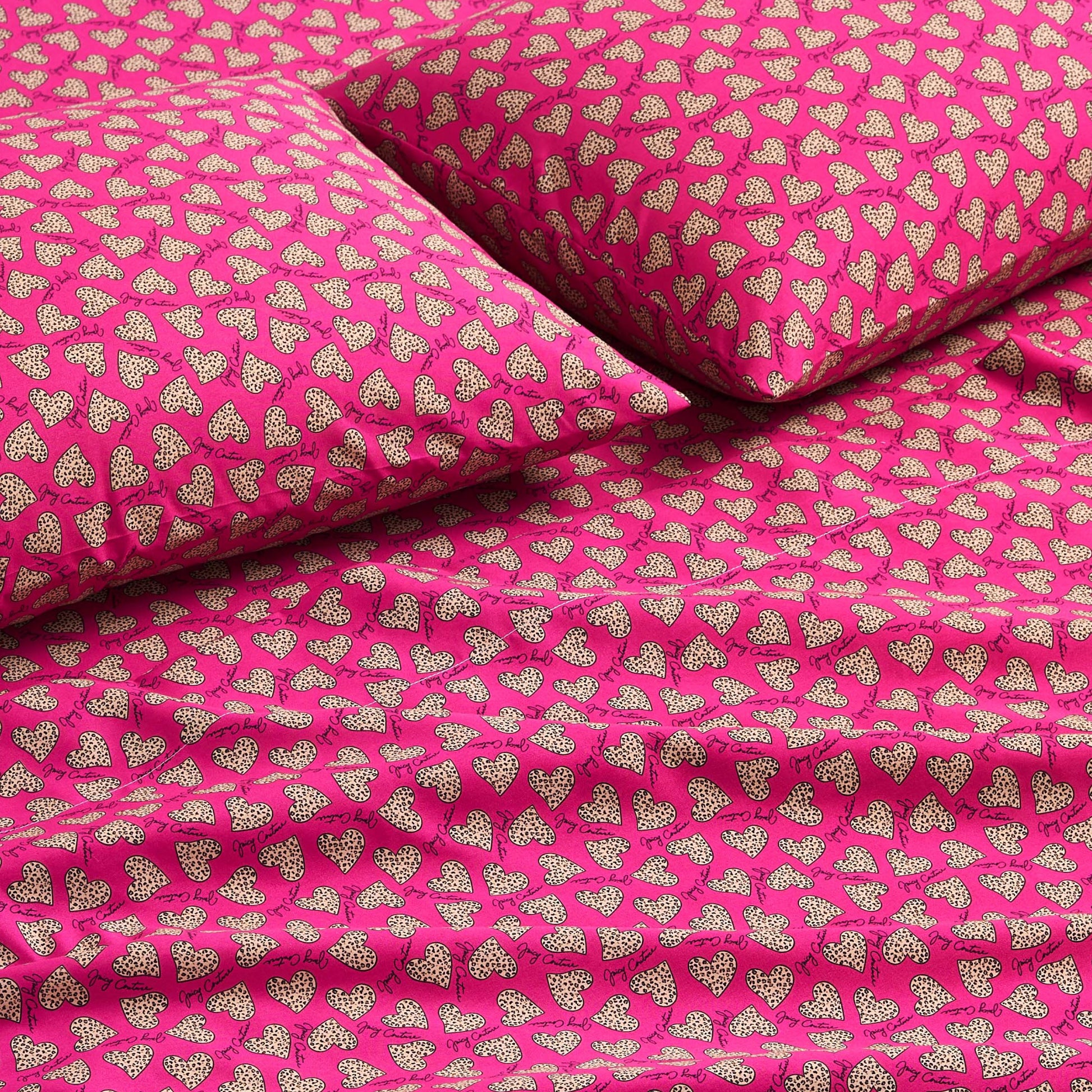 Close-up of a bed with a Printed Microfiber Sheet Set in bright pink, showcasing smooth fabric and a repeating pattern of small white polka-dotted hearts on the pillows and sheets—a vibrant, luxurious bedding accent.