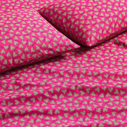 Close-up of a bed with a Printed Microfiber Sheet Set in bright pink, showcasing smooth fabric and a repeating pattern of small white polka-dotted hearts on the pillows and sheets—a vibrant, luxurious bedding accent.