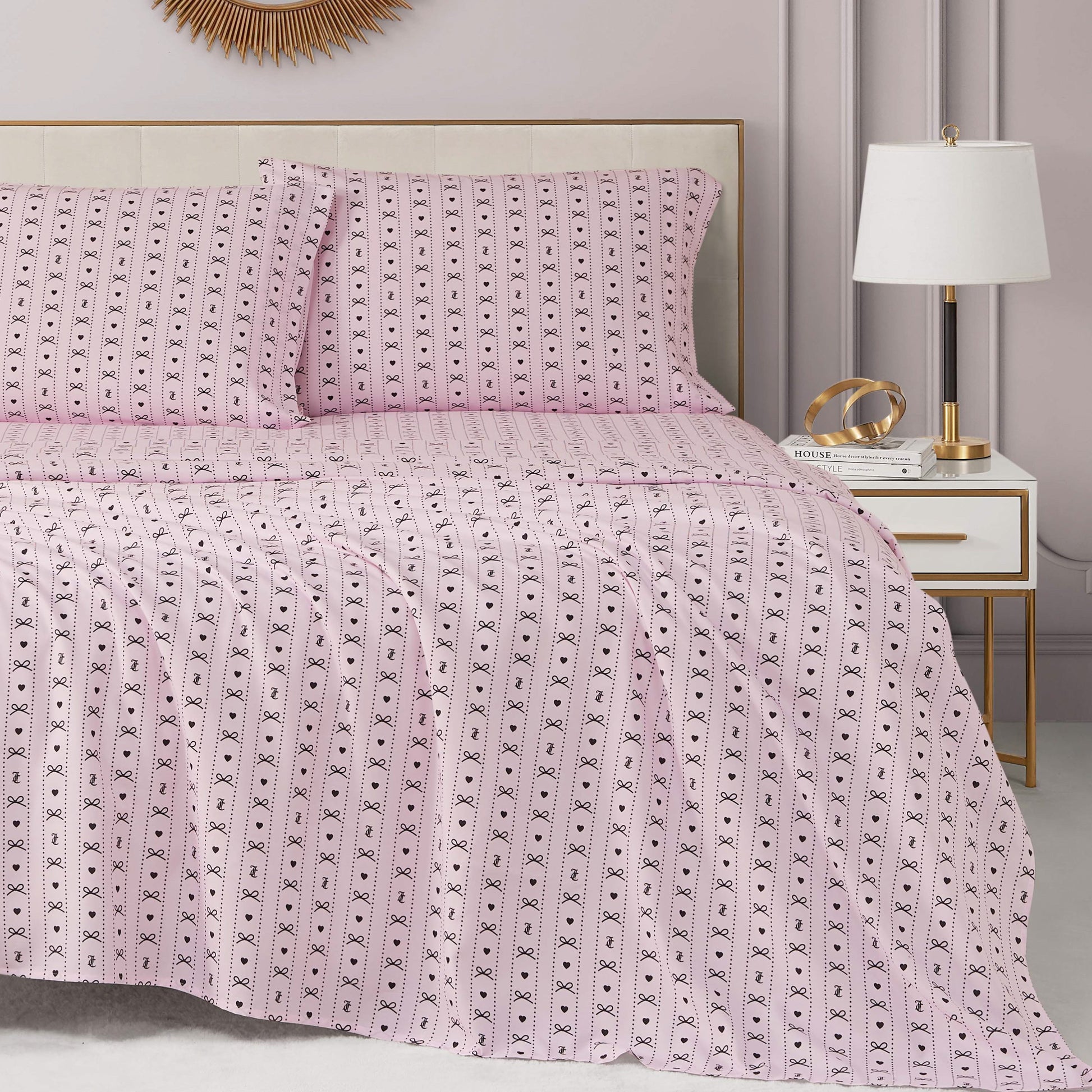 A neatly made bed with a Printed Microfiber Sheet Set and matching pillows sits beside a white nightstand holding a lamp, books, and gold decor in a modern, softly lit bedroom.