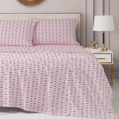 A neatly made bed with a Printed Microfiber Sheet Set and matching pillows sits beside a white nightstand holding a lamp, books, and gold decor in a modern, softly lit bedroom.