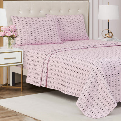 A neatly made bed with a Printed Microfiber Sheet Set in pink patterns and two matching pillows stands in a stylish bedroom. A nightstand with pink flowers, a lamp, and books adds to the modern, elegant luxury bedding decor.