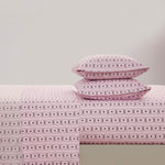 Two pink pillows on a bed with matching sheets, all displaying a black geometric and X pattern from the Printed Microfiber Sheet Set, create an elegant look against a plain light gray wall.