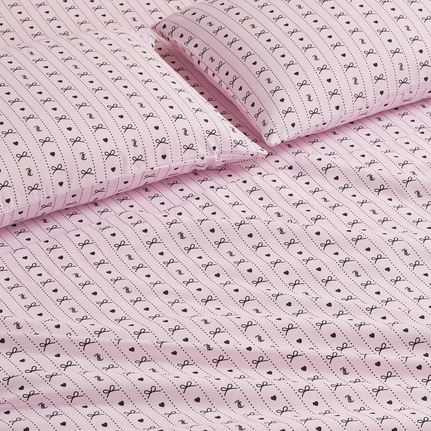 The Printed Microfiber Sheet Set features pink sheets and pillowcases adorned with small black bows, dots, and lines for a playful, delicate touch—perfect for adding charm and luxury to your bedroom décor.