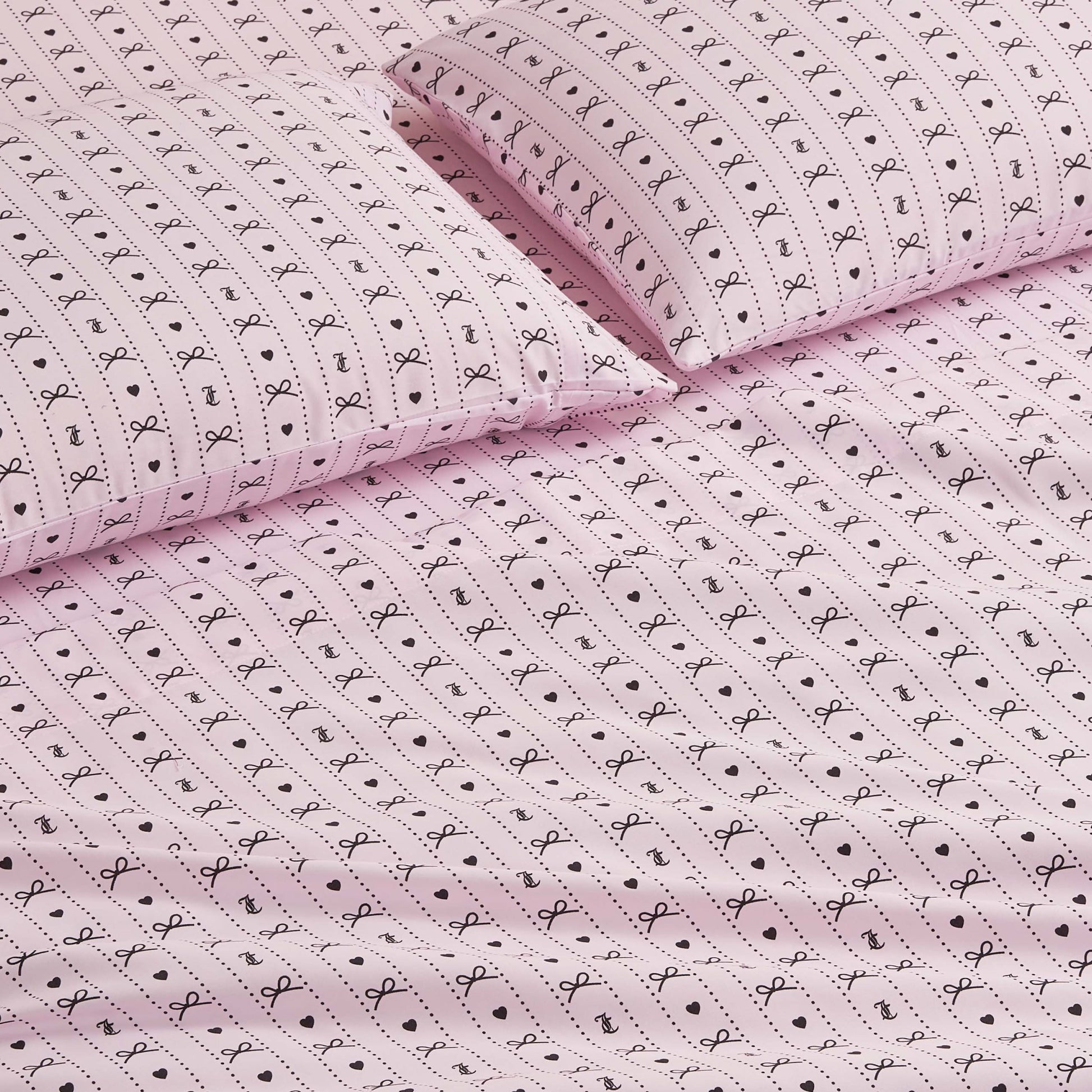 The Printed Microfiber Sheet Set features pink sheets and pillowcases adorned with small black bows, dots, and lines for a playful, delicate touch—perfect for adding charm and luxury to your bedroom décor.