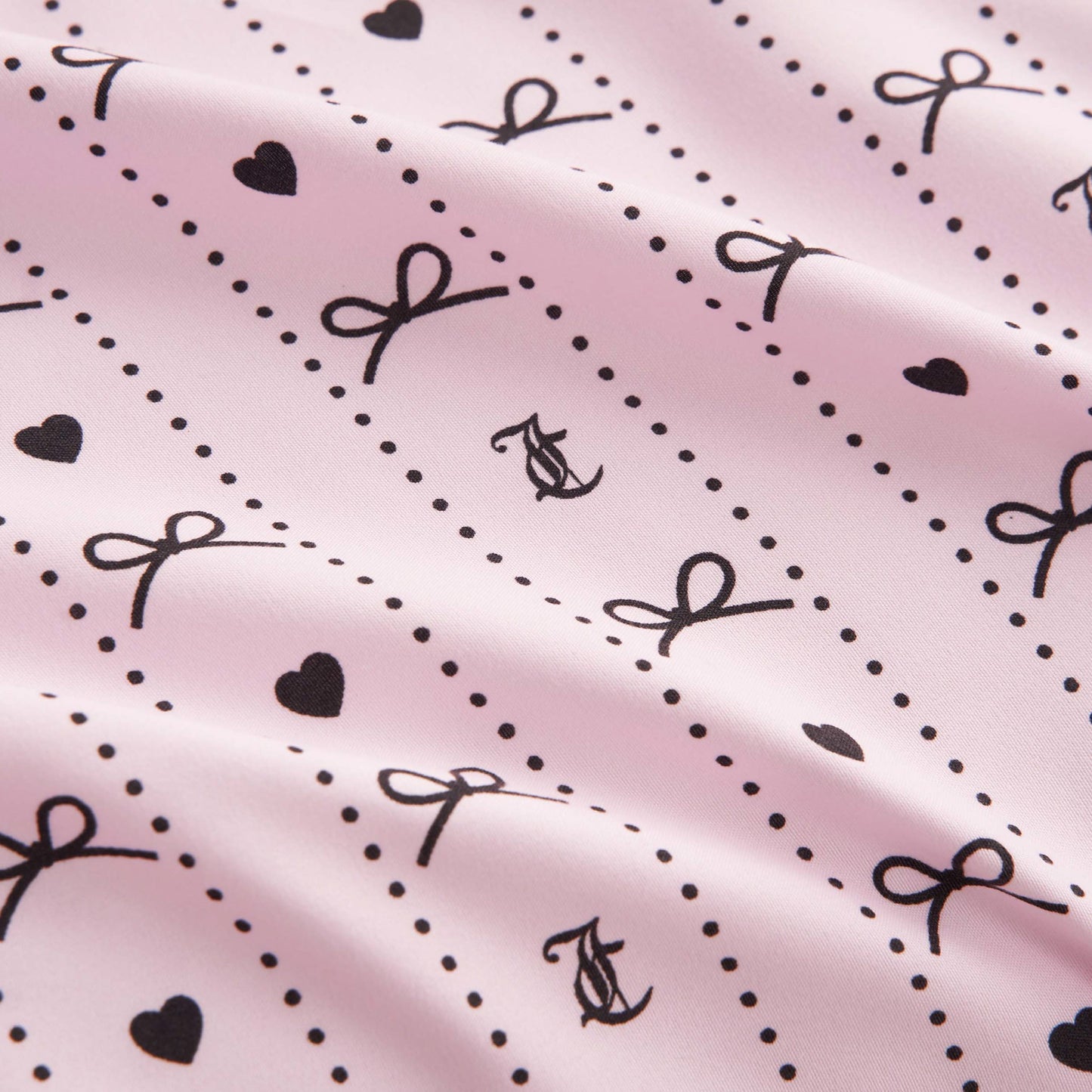The Printed Microfiber Sheet Set features a light pink design with black hearts, dots, bows, and intertwined “A” and “C”. Its softly wrinkled texture offers a gentle, wavy look for chic bedroom style.