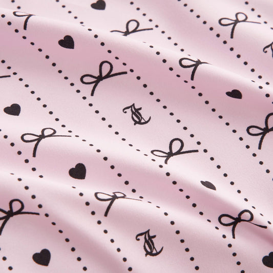 The Printed Microfiber Sheet Set features a light pink design with black hearts, dots, bows, and intertwined “A” and “C”. Its softly wrinkled texture offers a gentle, wavy look for chic bedroom style.