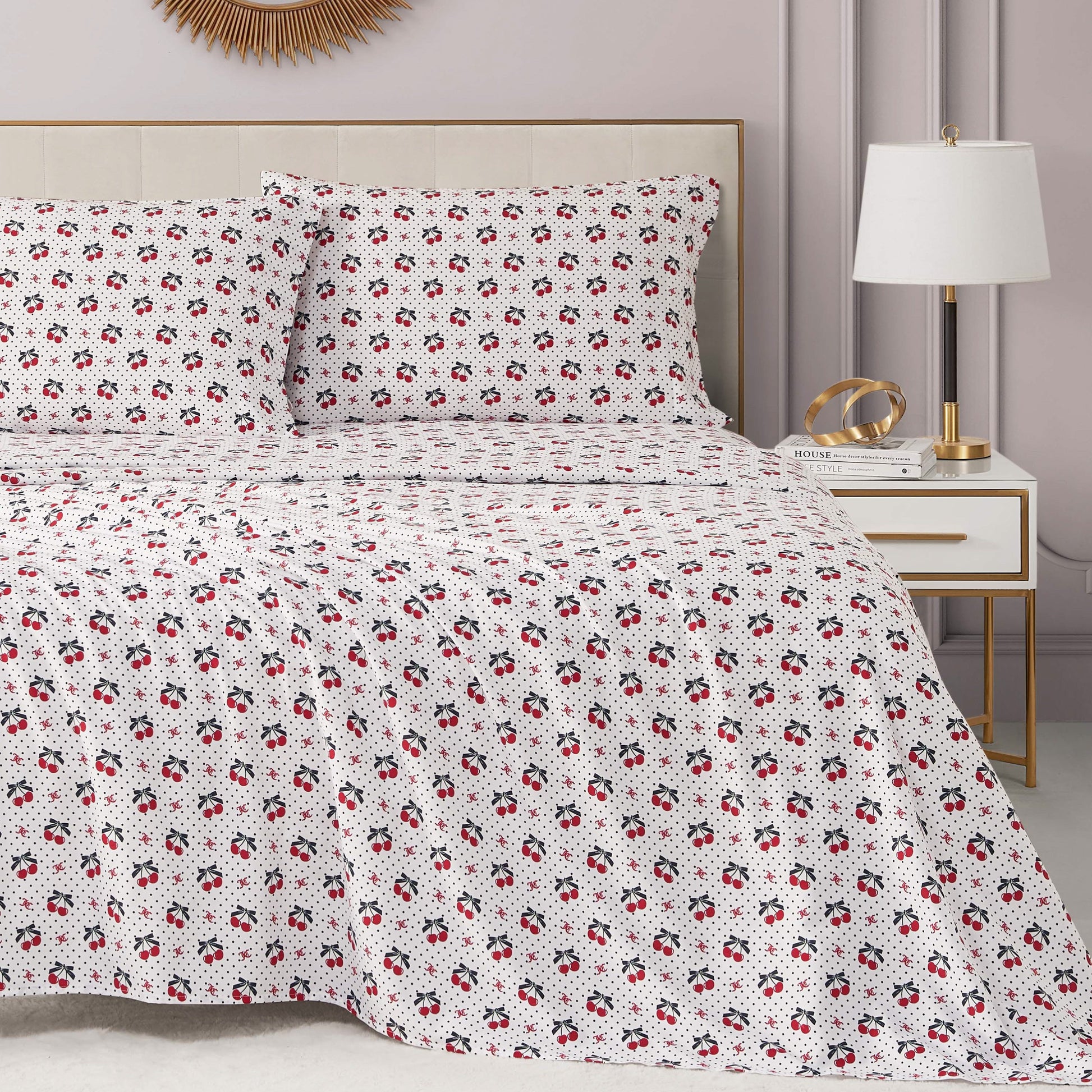 A neatly made bed features the Printed Microfiber Sheet Set with a subtle red and black floral design, adding a luxe touch. Beside it, a modern nightstand holds a lamp, books, and gold decor. The room is finished with soft neutral walls.