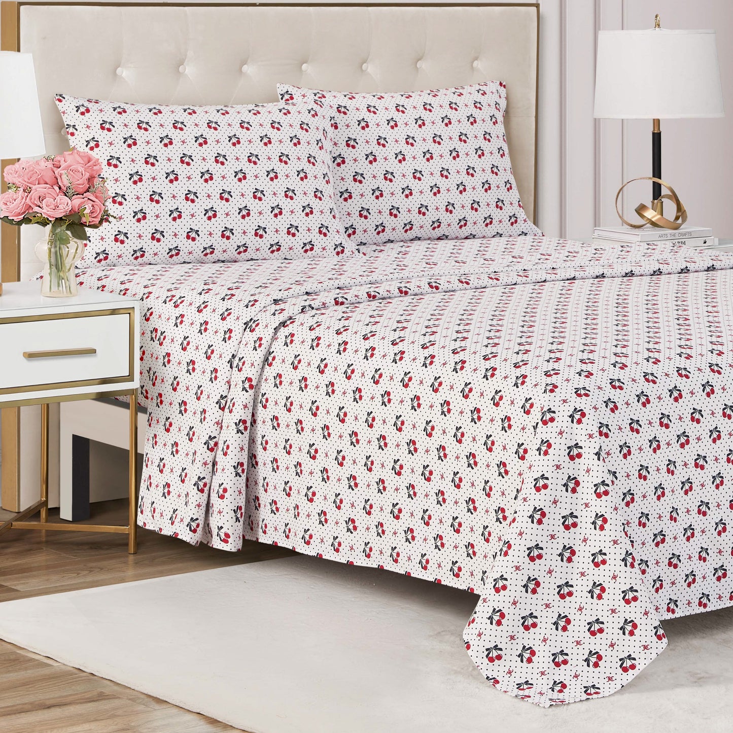 Showcase your luxury bedding style with the Printed Microfiber Sheet Set, featuring a white quilt and pillowcases with a red and black floral print, paired with a modern nightstand topped with pink flowers and a glowing lamp.