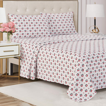 Showcase your luxury bedding style with the Printed Microfiber Sheet Set, featuring a white quilt and pillowcases with a red and black floral print, paired with a modern nightstand topped with pink flowers and a glowing lamp.