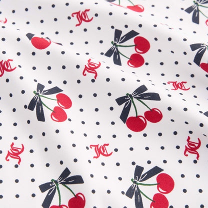 The Printed Microfiber Sheet Set features white fabric with small black polka dots, red cherries tied with black bows, and scattered red KC initials for a playful Juicy Couture touch. Slightly wrinkled for relaxed luxury bedding style.