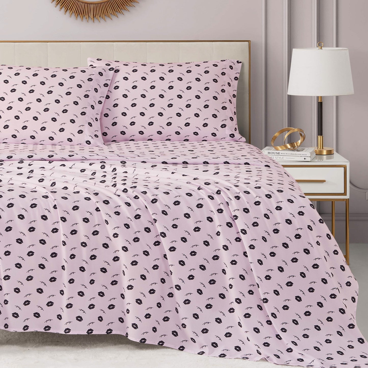 A neatly made bed with a light pink Printed Microfiber Sheet Set featuring a small black floral pattern, next to a white nightstand with a lamp and decor in a modern, pastel-toned bedroom.
