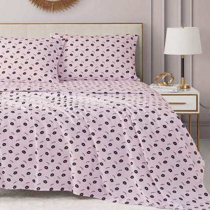 A neatly made bed with a light pink Printed Microfiber Sheet Set featuring a small black floral pattern, next to a white nightstand with a lamp and decor in a modern, pastel-toned bedroom.