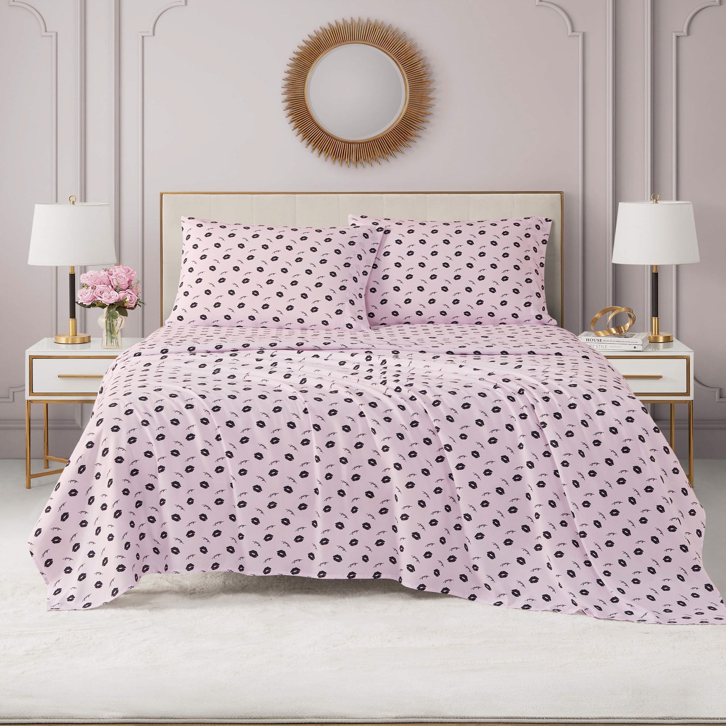 A neatly made bed with light pink Printed Microfiber Sheet Set featuring black polka dots, flanked by white nightstands with lamps and flowers, set against an elegant wall with molding and a round mirror above the headboard.