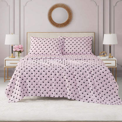 A neatly made bed with light pink Printed Microfiber Sheet Set featuring black polka dots, flanked by white nightstands with lamps and flowers, set against an elegant wall with molding and a round mirror above the headboard.