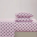 A neatly made bed with a light pink Printed Microfiber Sheet Set featuring black lips print pillowcases, set against a plain white background.