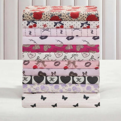 Eight Printed Microfiber Sheet Sets with colorful patterns—including roses, cherries, bows, hearts, lips, animal print, and butterflies—are neatly stacked against a light vertical-striped background for a luxurious bedding style.