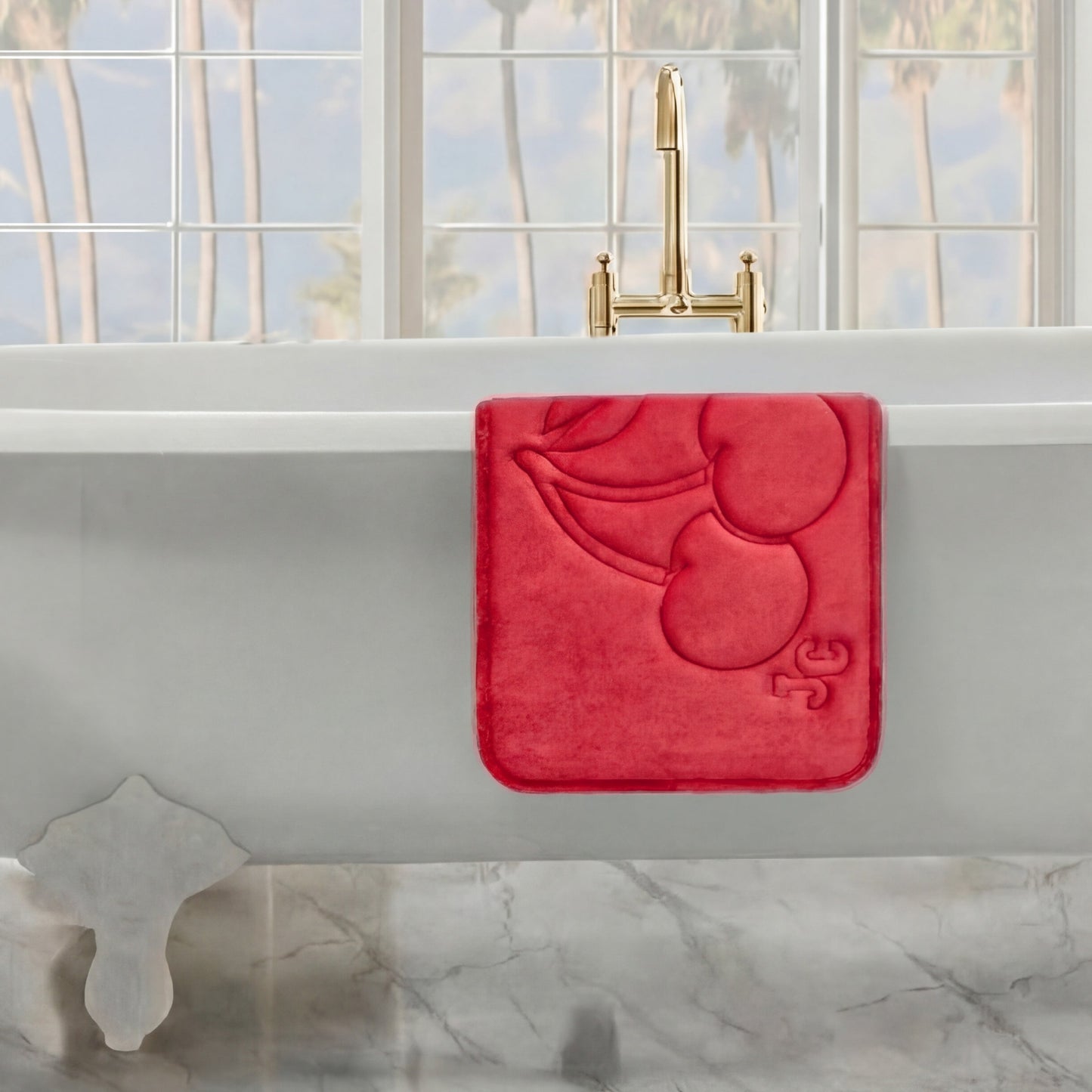 A Quilted Memory Foam Bath Mat is draped over the edge of a white tub beneath a gold faucet, with large windows and palm trees in the background, adding comfort and style to this luxurious bathroom setting.