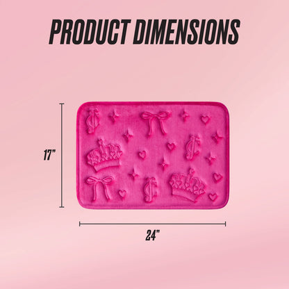 A rectangular pink Quilted Memory Foam Bath Mat with embossed crowns, bows, hearts, and dollar signs. Measures 17" x 24". "Product Dimensions" is printed above this luxurious bath mat.