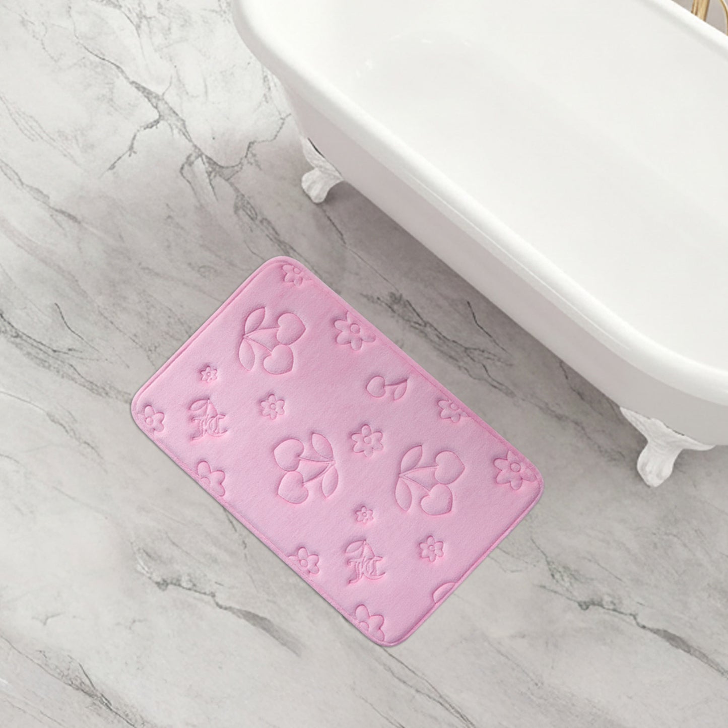 A pink rectangular Quilted Memory Foam Bath Mat with embossed floral and leaf patterns sits on a light gray marble floor beside a white clawfoot bathtub, adding style and offering a skid-resistant surface.
