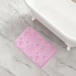 A pink rectangular Quilted Memory Foam Bath Mat with embossed floral and leaf patterns sits on a light gray marble floor beside a white clawfoot bathtub, adding style and offering a skid-resistant surface.